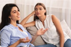 Donne sedute sul divano, una guarda con invidia l'altra che parla sorridente