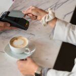 donna con davanti un cappuccino che paga con il bancomat