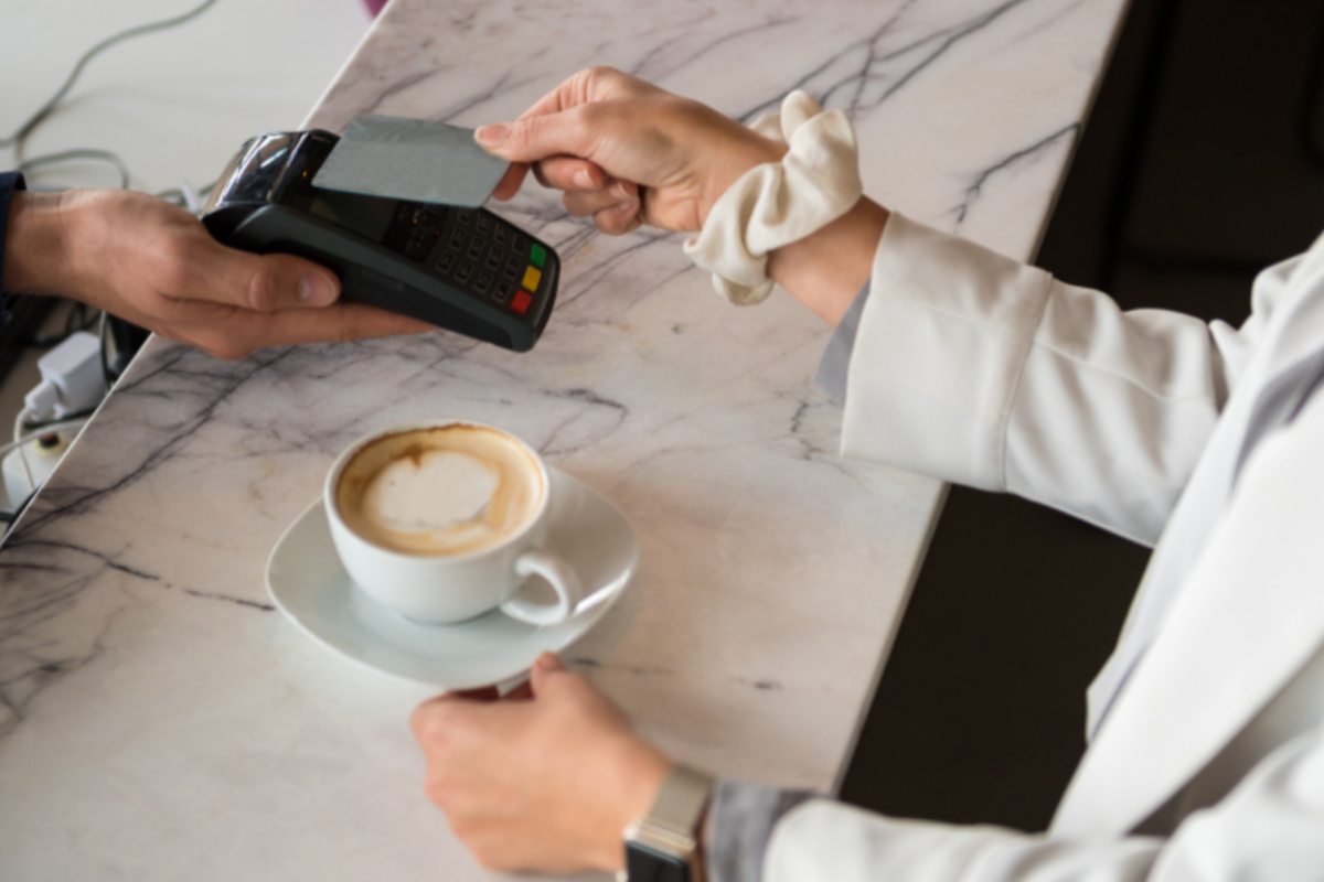donna con davanti un cappuccino che paga con il bancomat