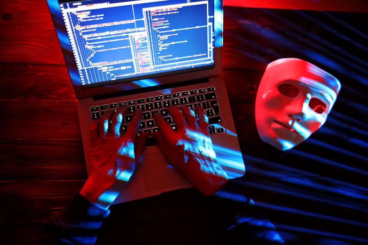 una persona che fa una truffa con il computer ed una maschera bianca vicino