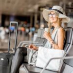 donna sorridente seduta in aeroporto con accanto una valigia