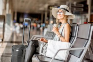 donna sorridente seduta in aeroporto con accanto una valigia